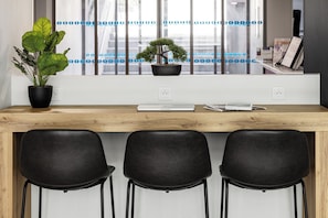 Un espace de travail moderne avec un bureau en bois, trois chaises noires, une plante en pot et une fenêtre avec des stores.