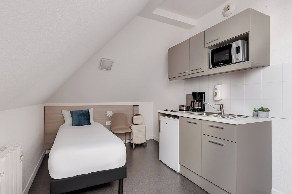 A compact room with a bed, kitchenette, and a small seating area.