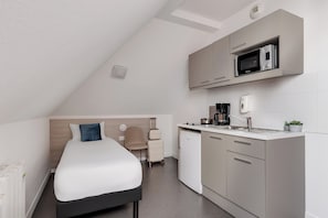 Une chambre compacte comprenant un lit, une kitchenette et un petit coin salon.