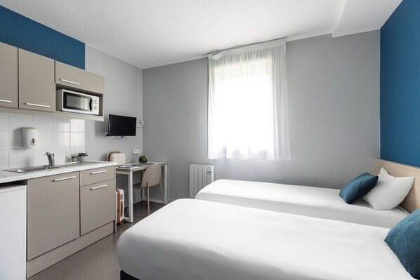 A hotel room with a kitchenette, a bed, a desk, and a TV.