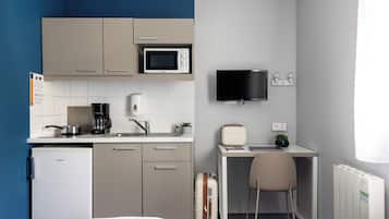 Habitación de hotel compacta con kitchenette, una cama, un escritorio con silla, un televisor y una maleta.