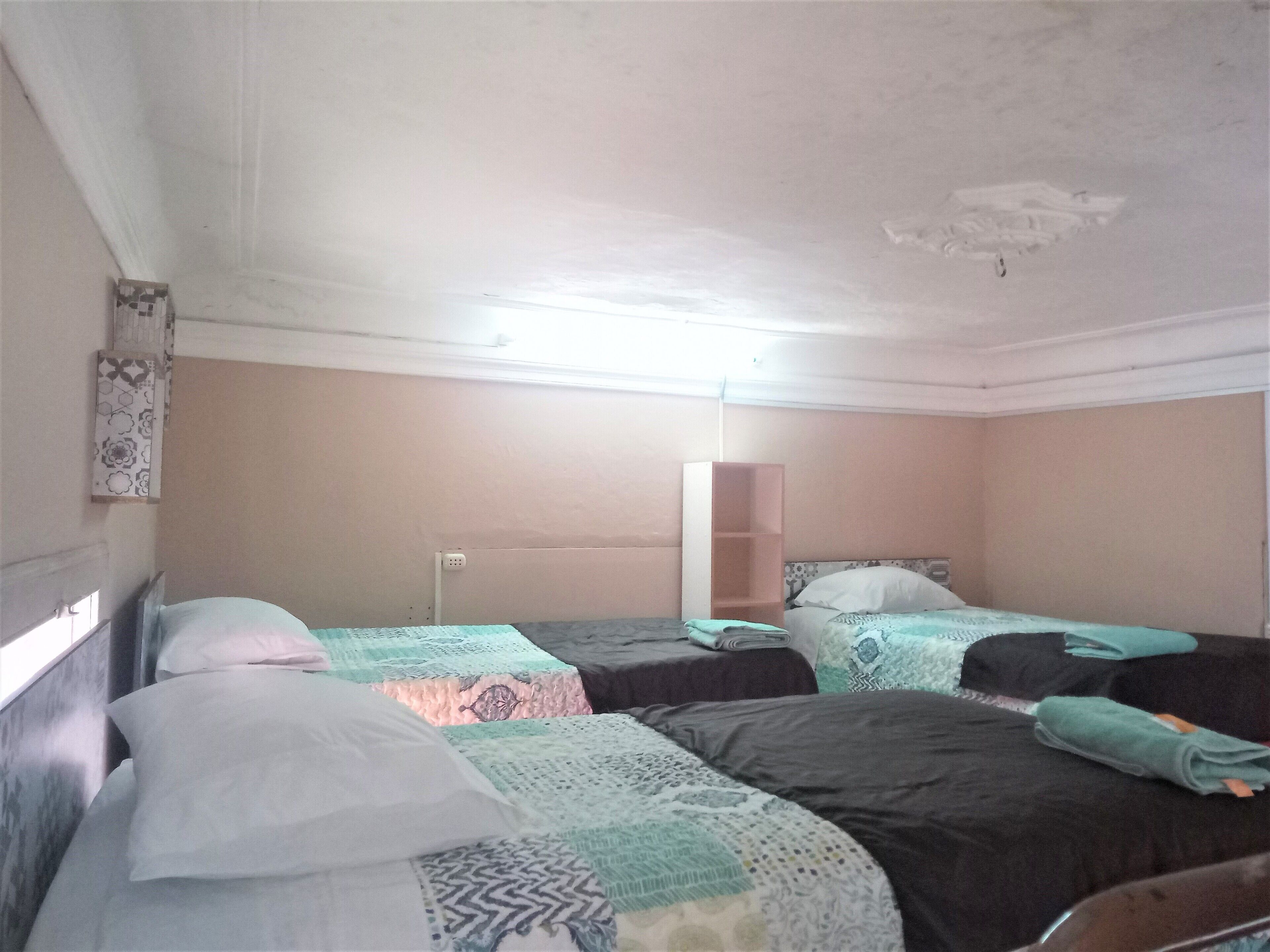 A room with three beds, each with a patterned bedspread. There is a white wall with a decorative panel and a mirror.