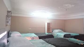 A room with three beds, each with a patterned bedspread. There is a white wall with a decorative panel and a mirror.