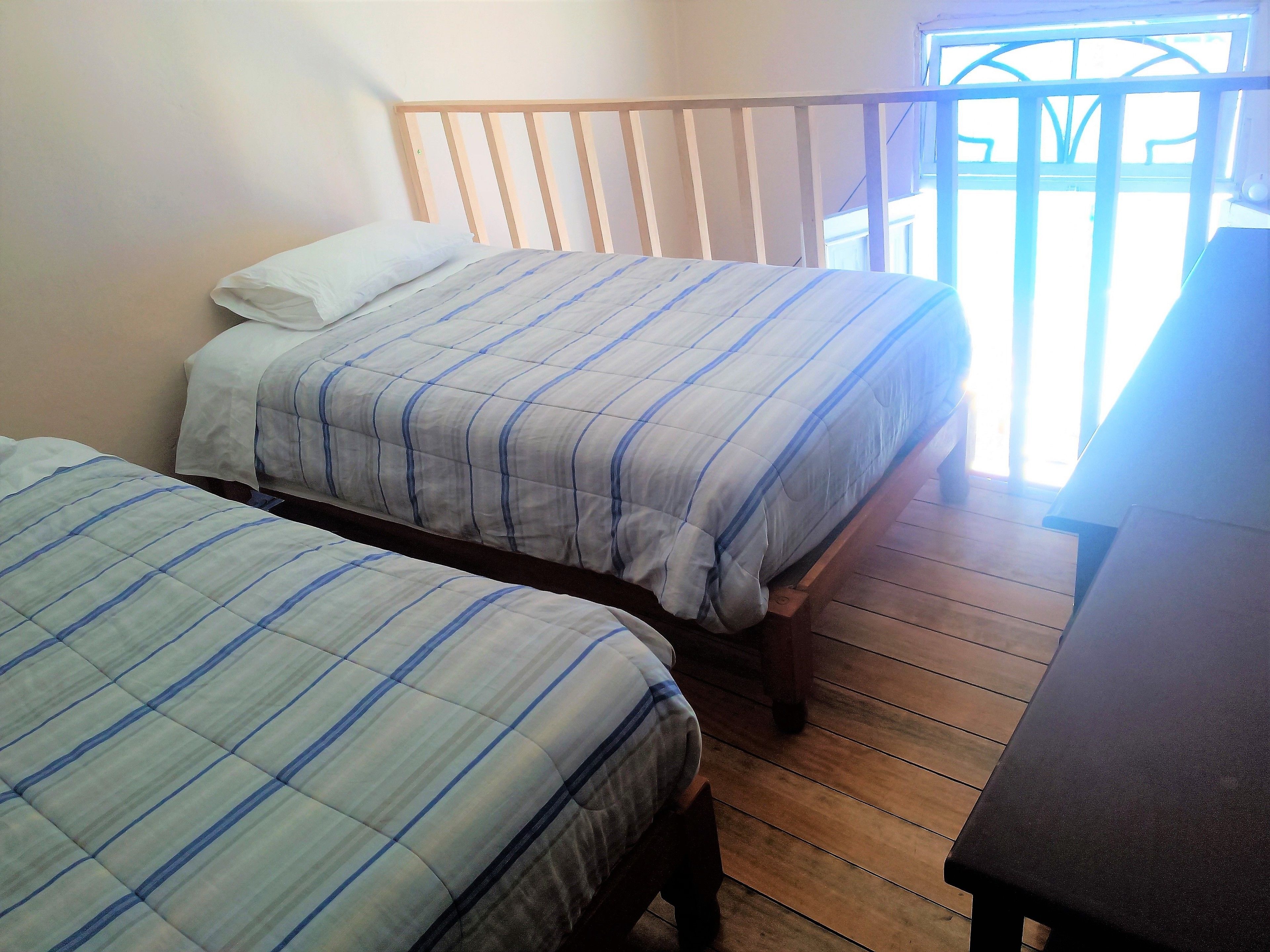 A room with two beds, wooden flooring, and a window with a view.