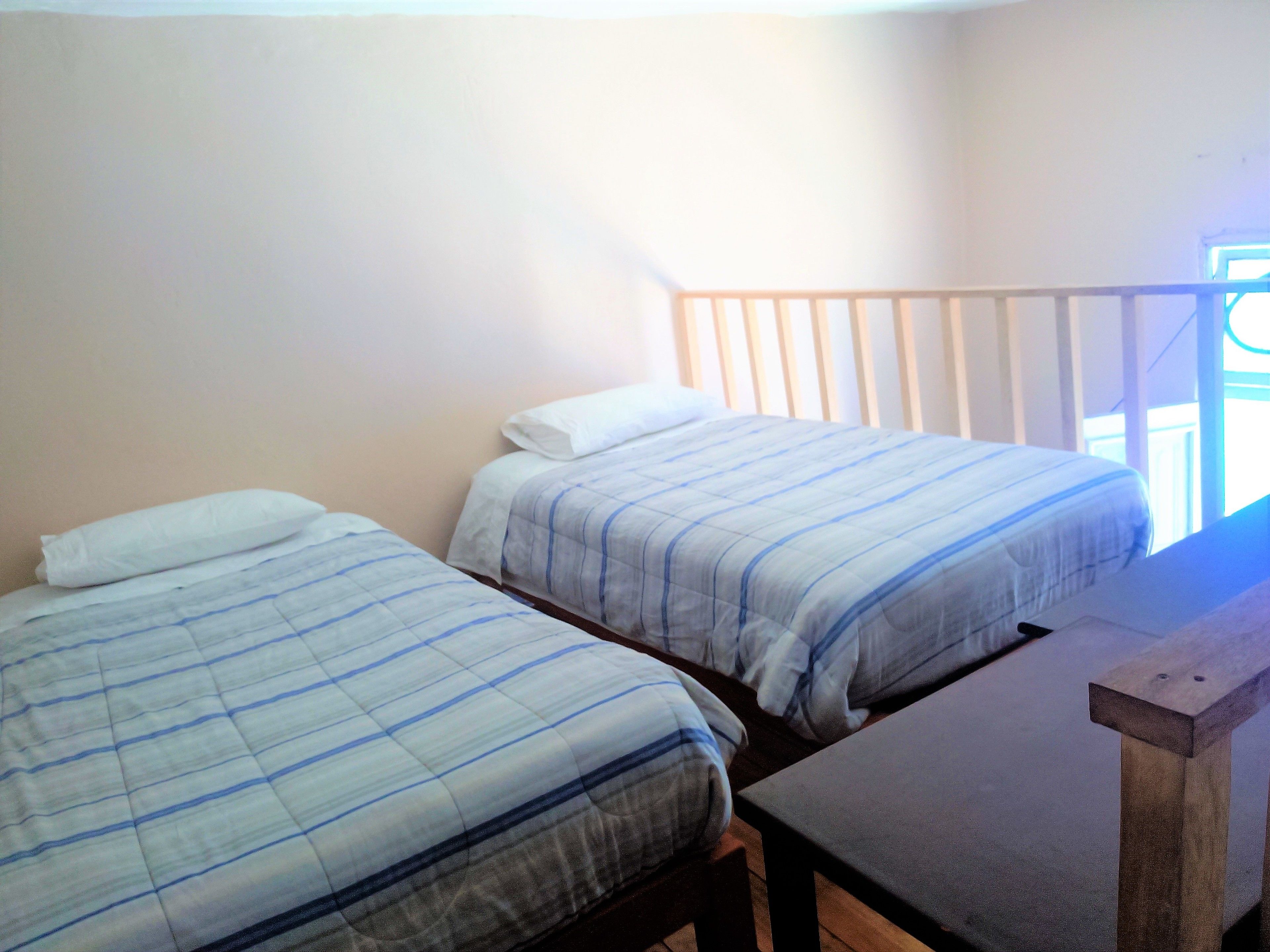 Deux lits simples avec du linge de lit à rayures, dans une pièce qui comprend un banc en bois et une fenêtre.