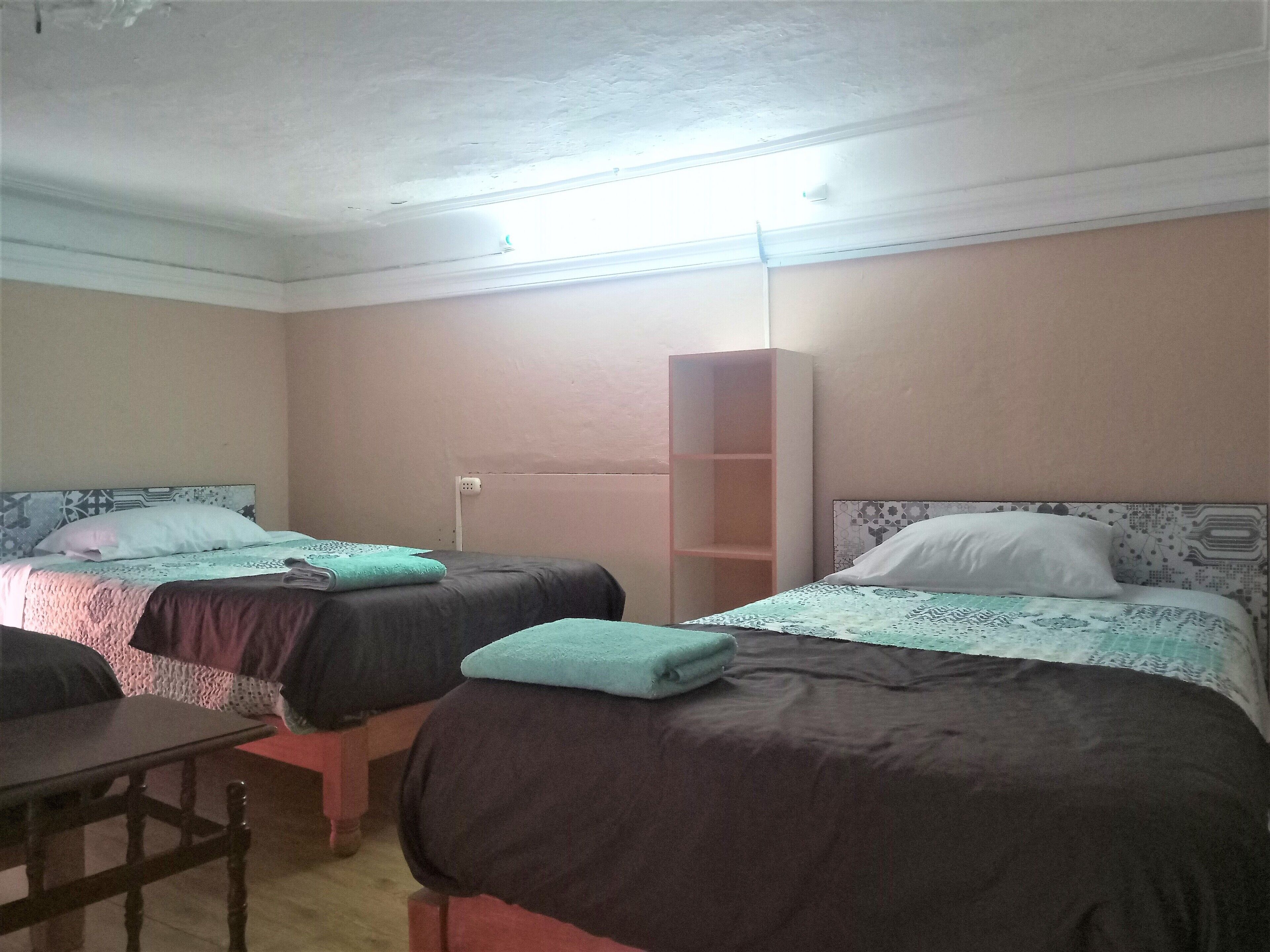 A room with two beds, a wooden table, and a tall wardrobe.