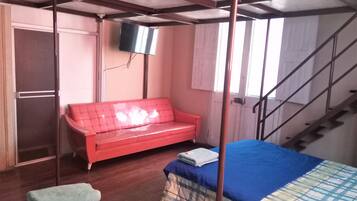 A room with a bed, a red sofa, a television mounted on the wall, and a staircase.