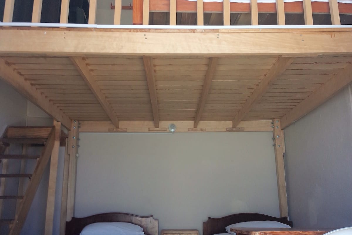 A dormitory room with two single beds, a wooden bunk bed above, a small wooden desk, and a chair.