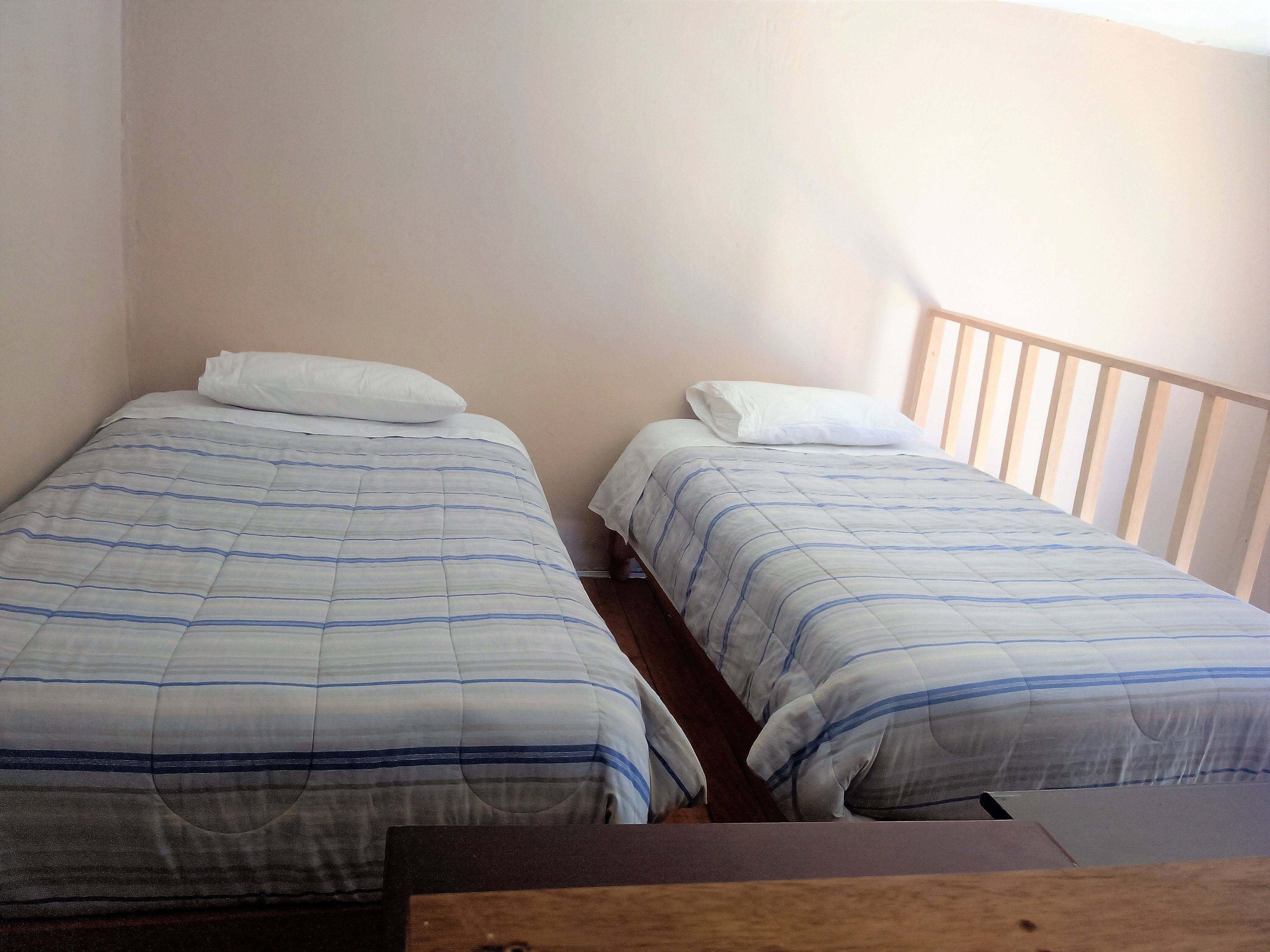 Una habitación pequeña con dos camas individuales, cada una con un almohadón blanco y una manta a rayas.