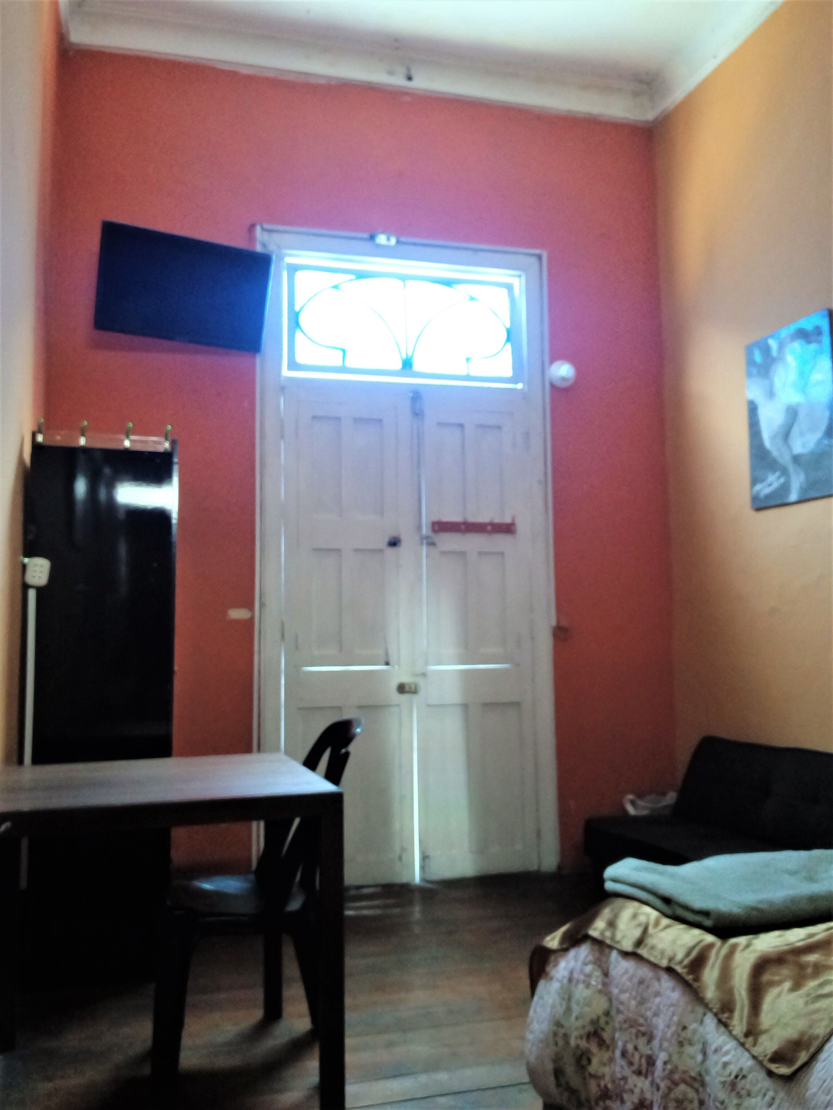 Una habitación con una puerta blanca, una mesita, una silla, un sofá negro y un cuadro en la pared.
