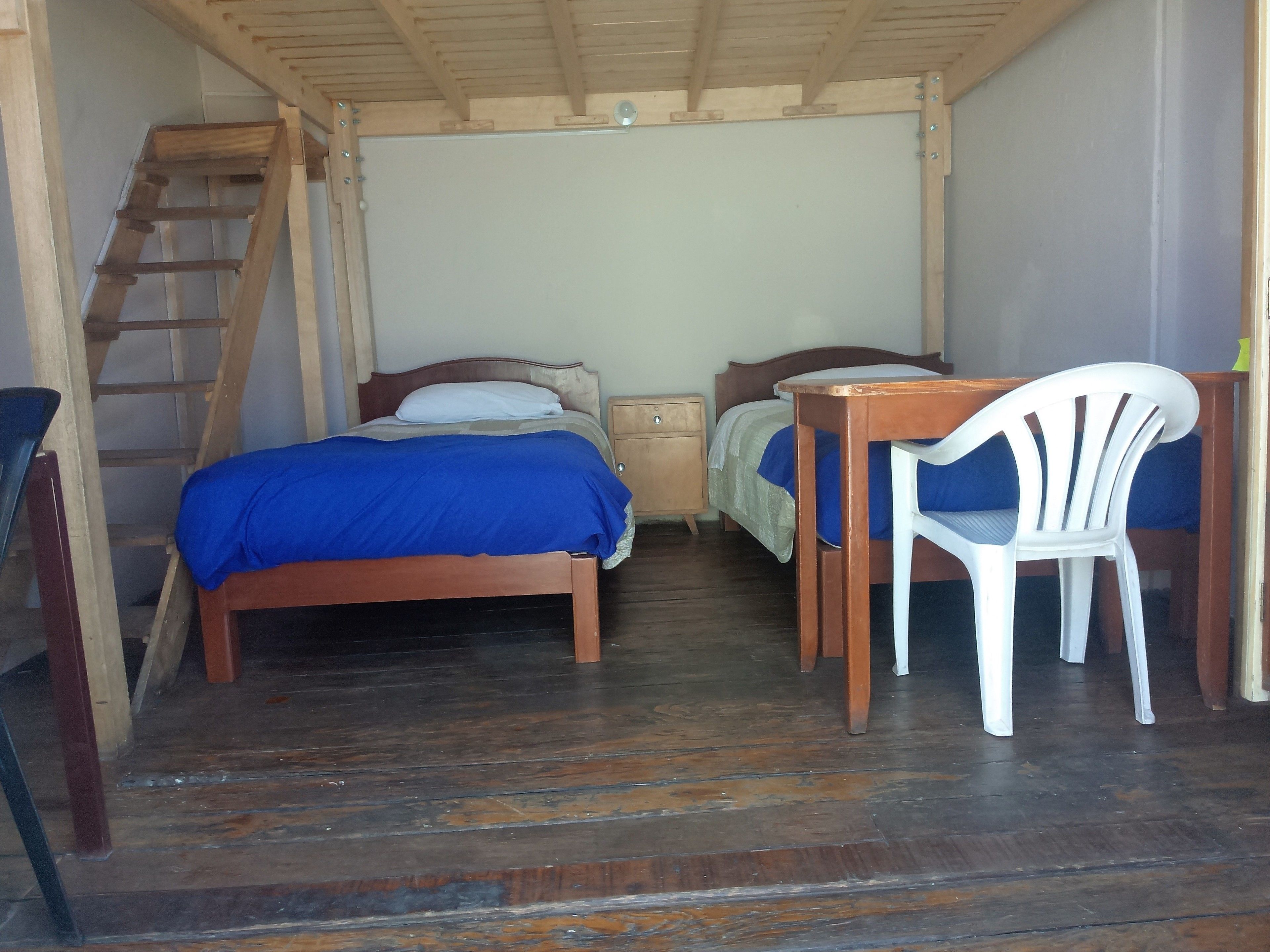 A room with two wooden beds, a desk with a chair, a ladder, and a small nightstand.