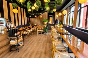 A restaurant interior with wooden tables and chairs, hanging plants, and a bar area with bottles. - Hotel Olimp (Cluj-Napoca)