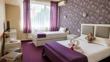 A hotel room with a bed, a bedside table, a TV, a window with curtains, and a floral wallpaper.