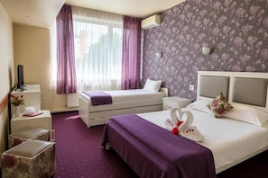 A hotel room with a bed, a bedside table, a TV, a window with curtains, and a floral wallpaper. - Hotel Olimp (Cluj-Napoca)