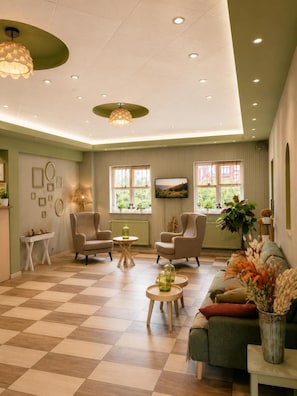 A spacious living room with a checkered floor, multiple seating options, and a large window offering a view of greenery. - Hotel Olimp (Cluj-Napoca)