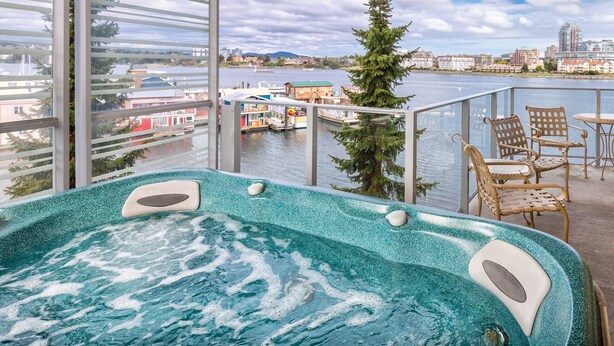Un balcón con bañera de hidromasaje, sillas y vistas a un río y un paisaje urbano.