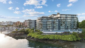 Un edificio moderno de varios pisos con balcones, cerca de un puerto deportivo con barcos.