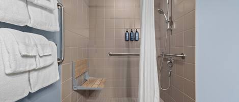 A shower area with a white shower curtain, a bench, and two bottles of shampoo.