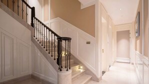 Una imponente escalera con paneles blancos y una base de mármol que conduce a un pasillo con piso de tonos claros.