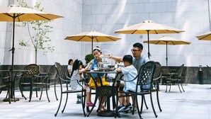 An outdoor dining area with tables and chairs, umbrellas, and a modern building in the background. - Wyndham Grand Xian Residence (Xi'an)