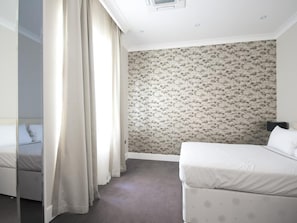A hotel room with a bed, a nightstand, a wall with floral wallpaper, and a window with curtains. - Chilworth Court (London)