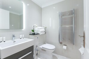 Un baño moderno con un espejo grande, un lavamanos blanco, un inodoro, una ducha y un perchero para toallas.