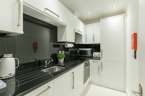 Una cocina moderna con armarios blancos, encimera negra, electrodomésticos de acero inoxidable y una pequeña planta en maceta.