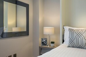 Habitació d'hotel amb un mirall gran, una taula de nit amb una làmpada, una foto amb marc i un coixí decoratiu.