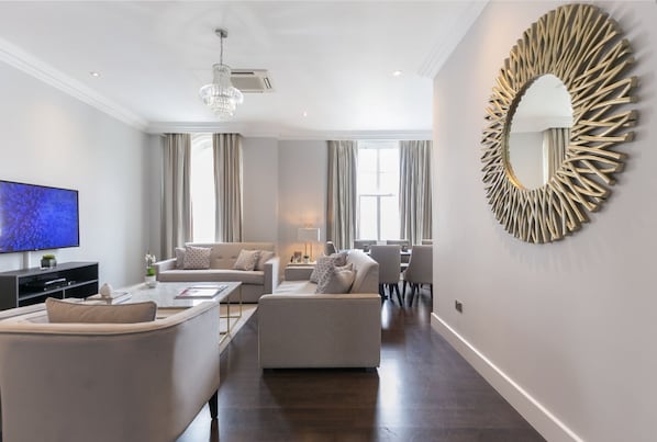A modern living room with a flat-screen TV, a chandelier, a round mirror, and a dining area. - Chilworth Court (London)