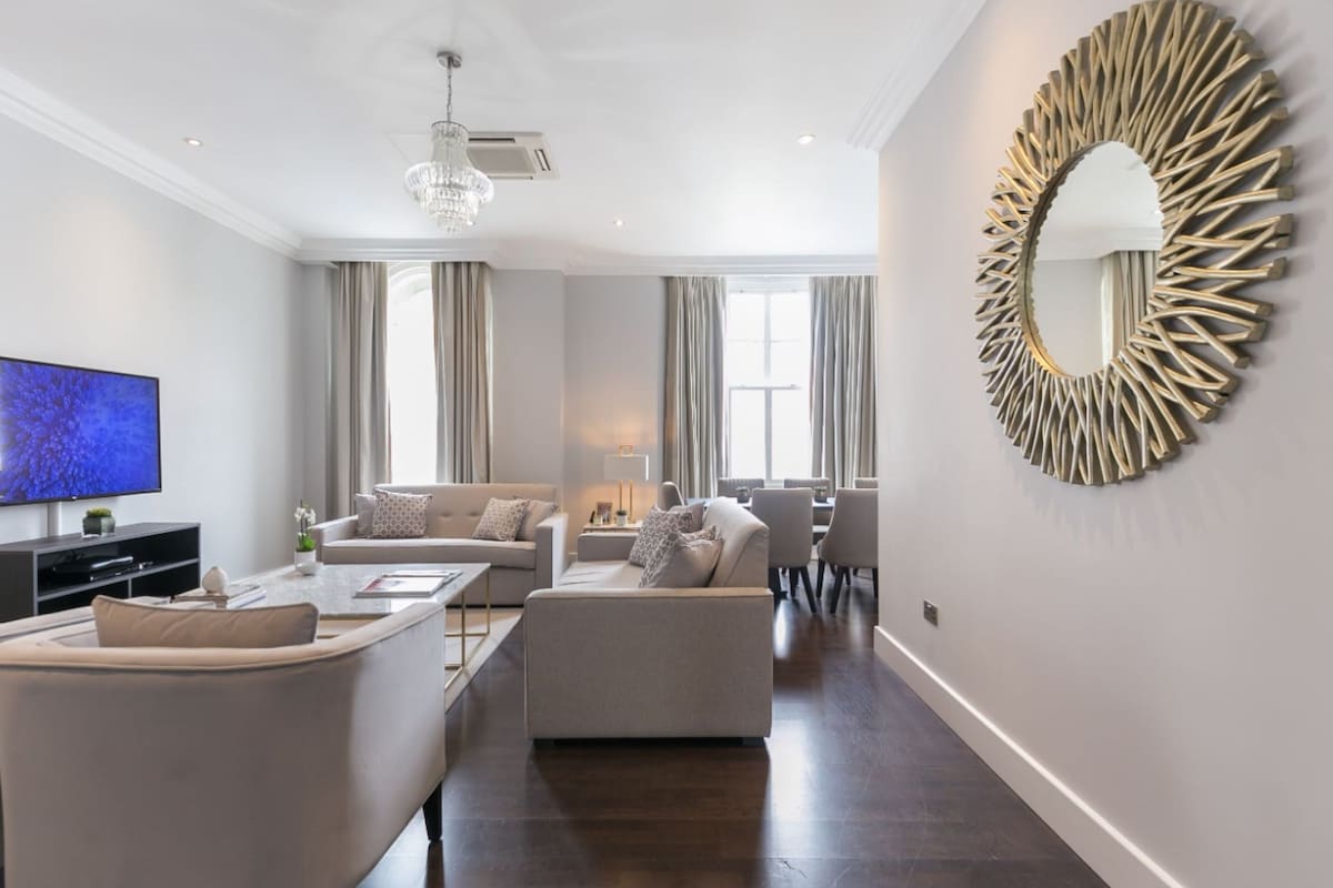 A modern living room with a flat-screen TV, a chandelier, a round mirror, and a dining area.