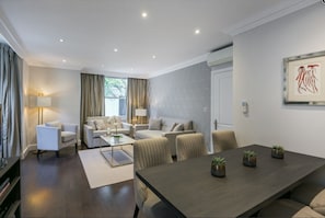 A modern living room with a sofa set, a dining table with potted plants, and a large window with curtains. - Chilworth Court (London)