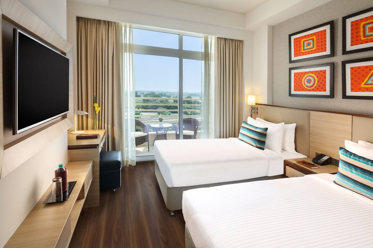 A hotel room with two beds, a TV, a desk, a chair, and a balcony with a view.
