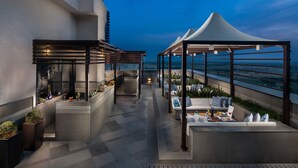 A rooftop terrace with outdoor seating, a bar area, and a view of the ocean. - Sandal Suites Op. by Lemon Tree Hotels (Noida)