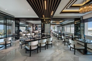 Un comedor moderno con varias mesas y sillas, ventanas amplias y un techo alto con luminarias lineales.