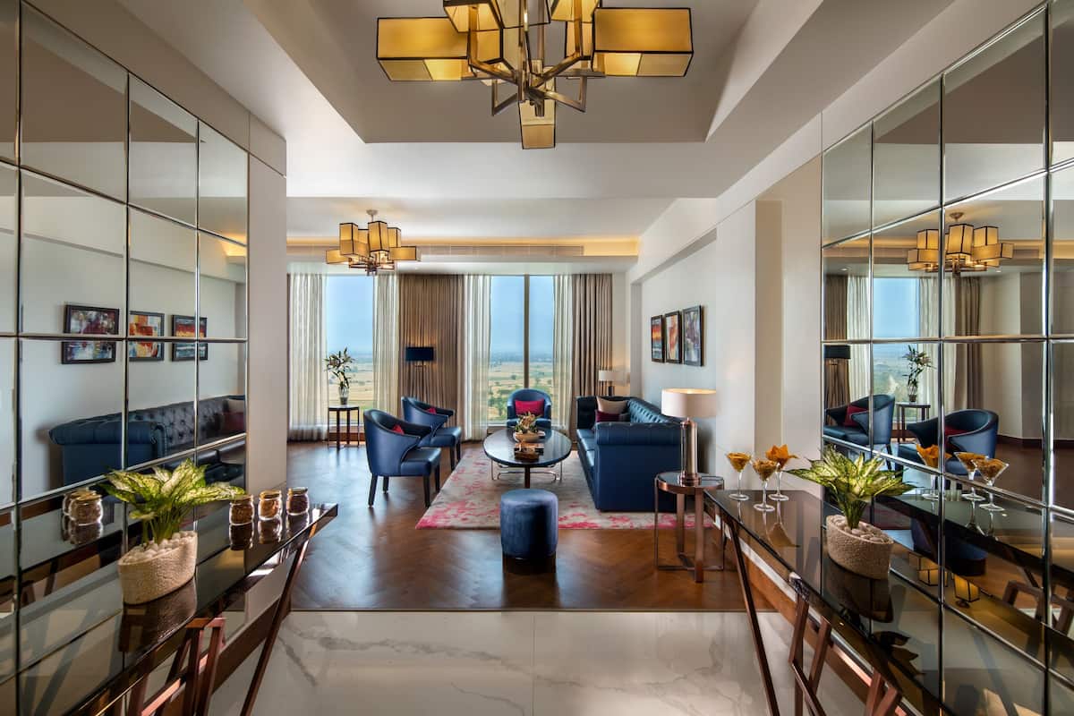 A spacious living area with a large window, a chandelier, and a dining table with chairs.
