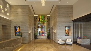 A modern lobby with a marble reception desk, two seating areas, and a colorful stained glass window. - Sandal Suites Op. by Lemon Tree Hotels (Noida)
