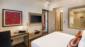 A modern hotel room with a bed, a desk with a computer, a TV, and a large mirror.