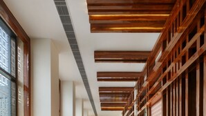 A hallway with wooden beams and a marble floor, leading to a bright room with a view. - Sandal Suites Op. by Lemon Tree Hotels (Noida)