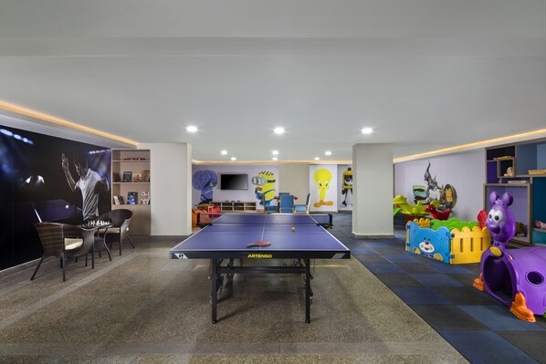 Una habitación amplia con mesa de ping pong, asientos cómodos y un área de juegos para niños.