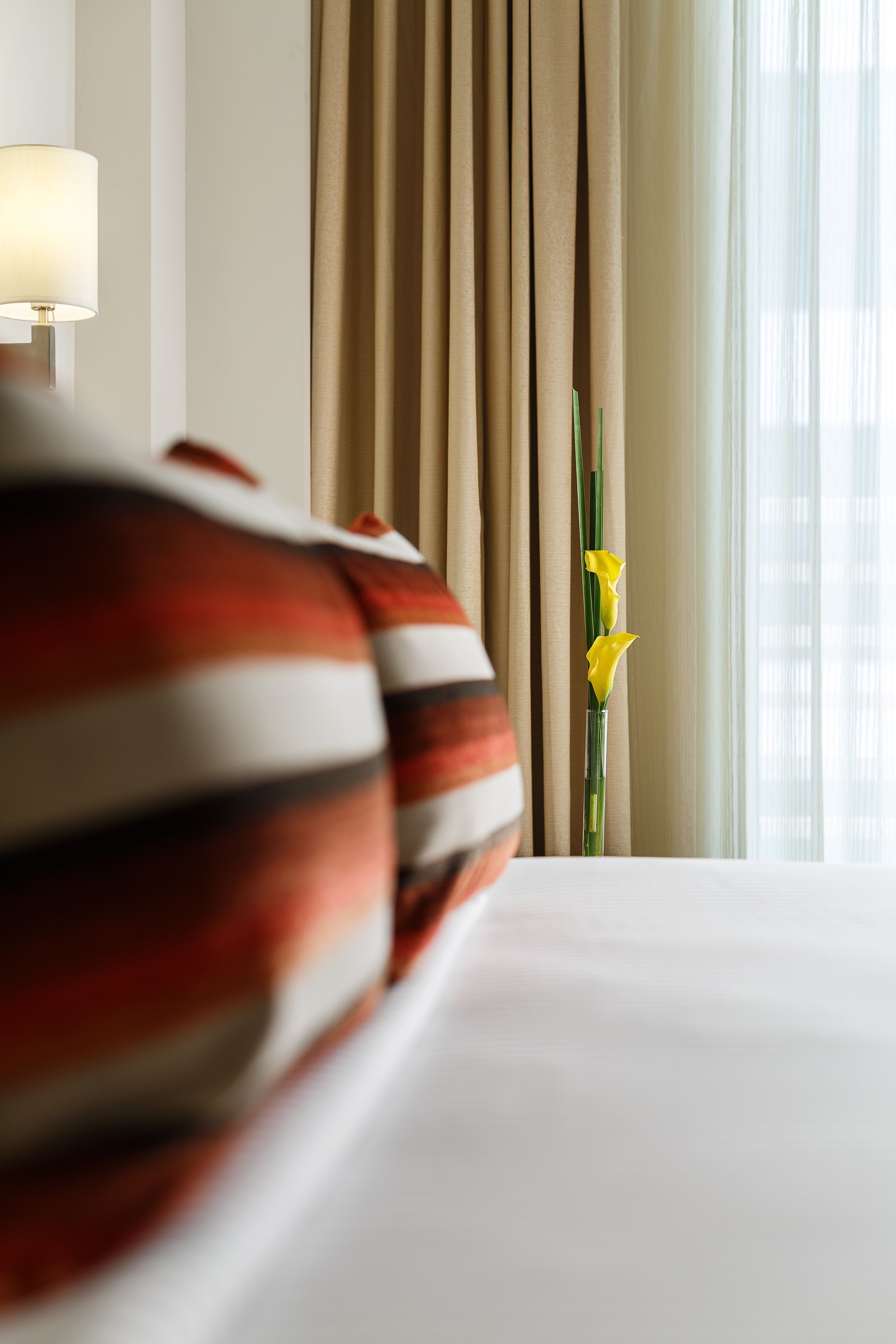 Une chambre d’hôtel avec un lit, des rideaux et un vase rempli de fleurs.