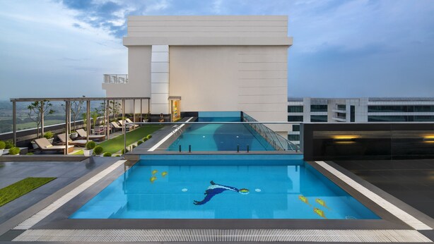 A modern hotel with a rooftop infinity pool, lounge area, and a view of the cityscape. - Sandal Suites Op. by Lemon Tree Hotels (Noida)
