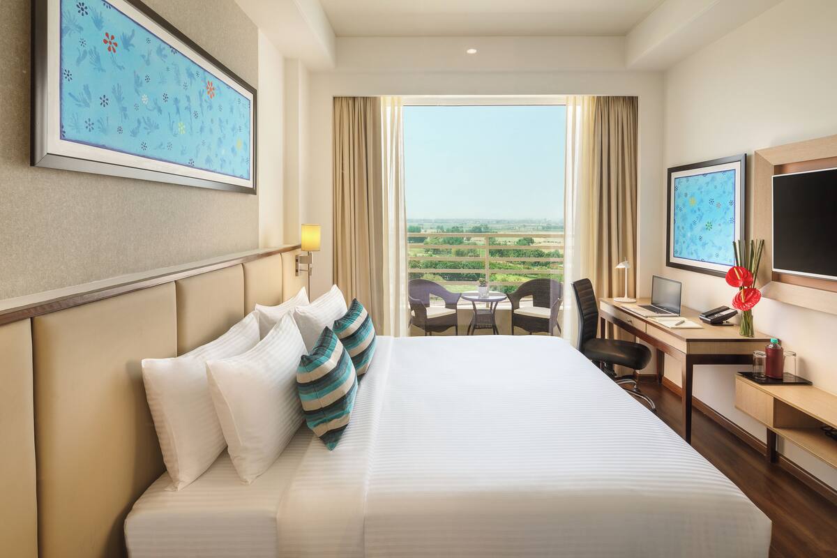 A hotel room with a large bed, a desk with a laptop, a chair, and a view of the landscape.
