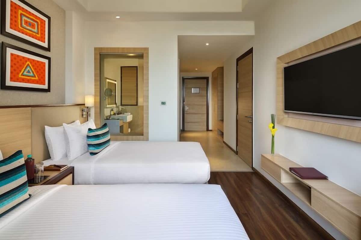 A hotel room with two beds, a TV, a desk, and a bathroom visible through an open door.