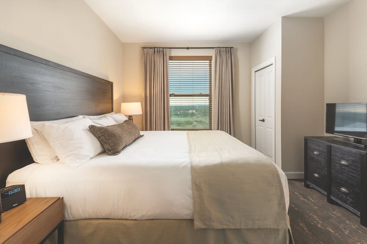 A hotel room with a bed, bedside lamps, a TV, and a window with curtains.