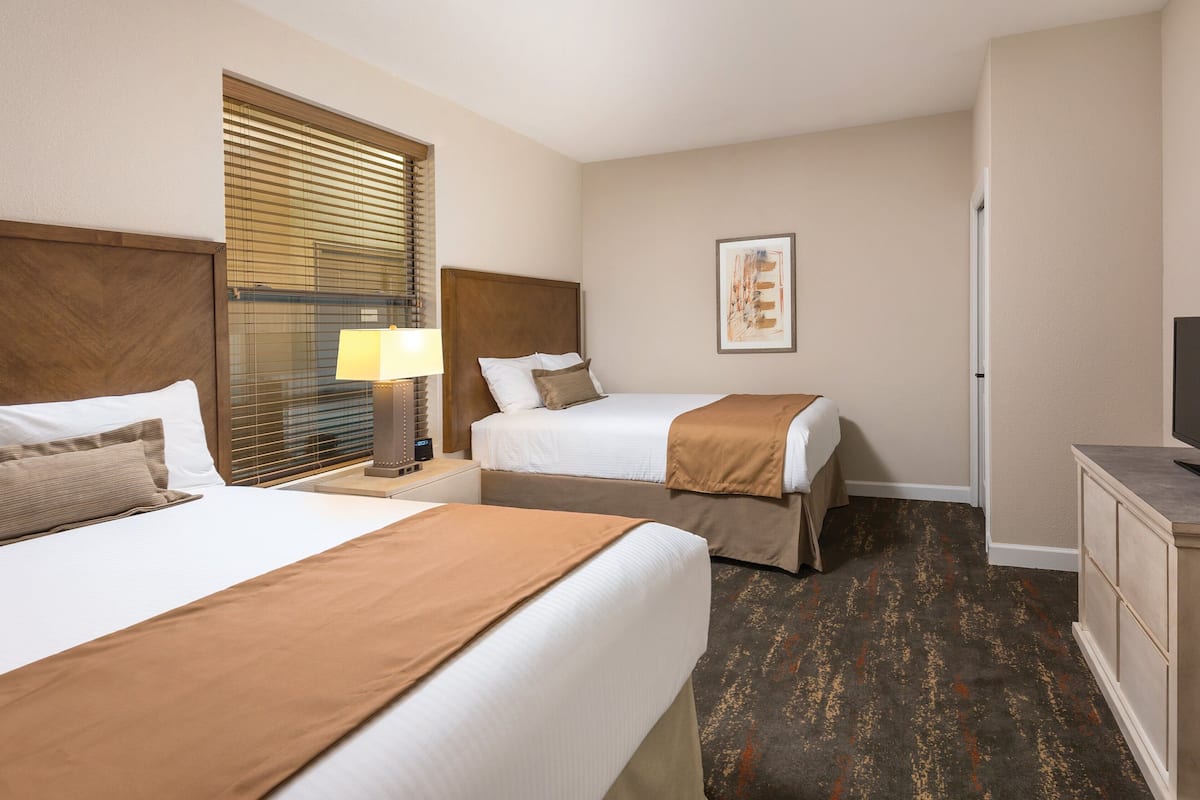 A hotel room with two beds, a TV, a lamp, and a painting on the wall.