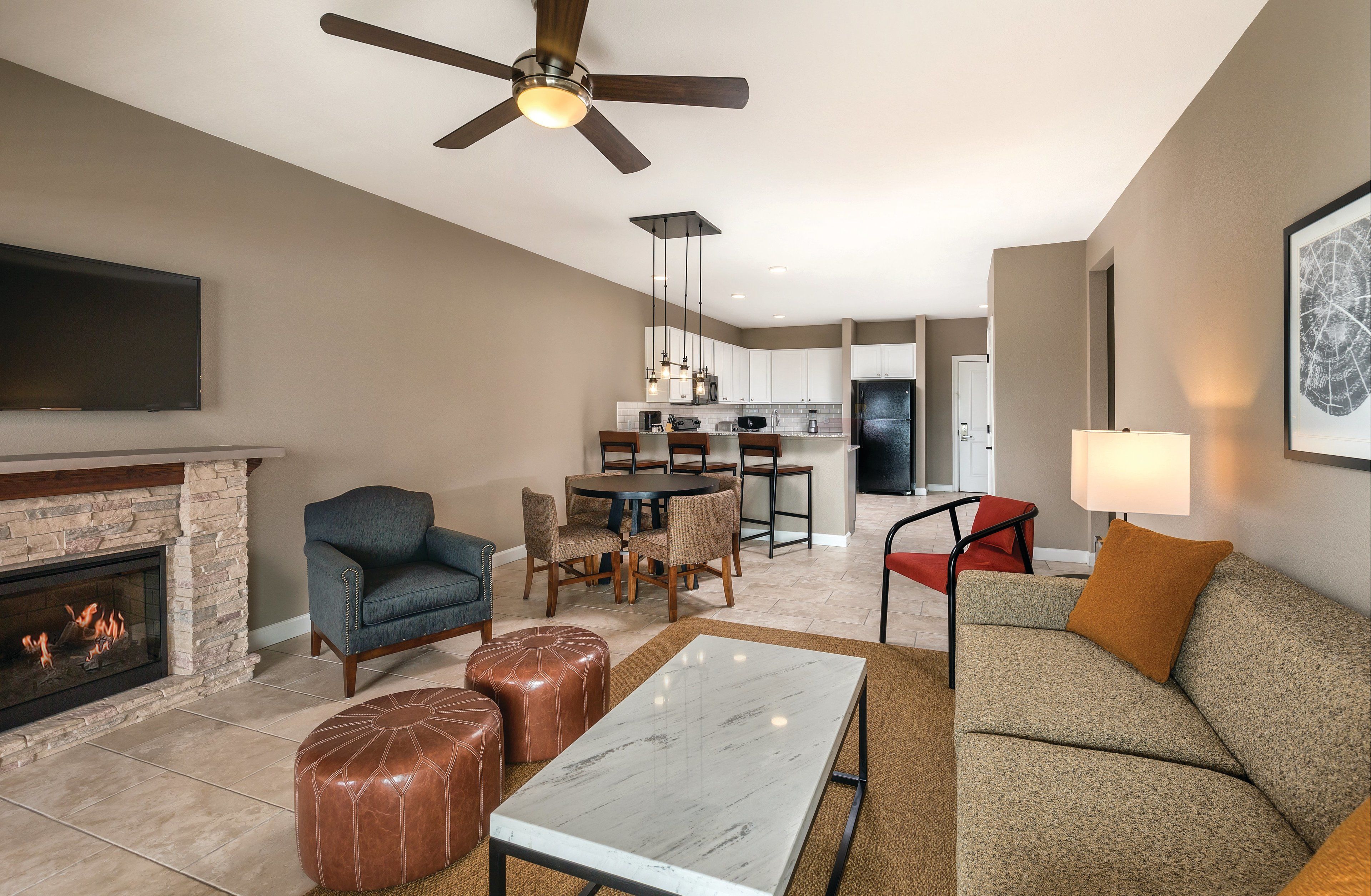 Una sala de estar moderna con chimenea, ventilador de techo, comedor y cocina al fondo.