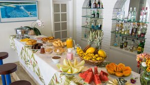 A breakfast buffet with tropical fruits, pastries, and beverages, and a bar area with liquor bottles. - Hotel Doce Mar (Búzios)