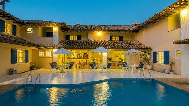 A pool area with lounge chairs and umbrellas, a bar, and a building with a tiled roof. - Hotel Doce Mar (Búzios)