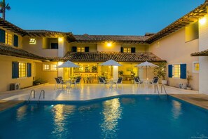 Zona de piscina amb gandules i ombrelles, un bar i un edifici amb teulada de rajola.