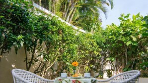 A table with a floral tablecloth and two wicker chairs in a garden with lush greenery and a palm tree. - Hotel Doce Mar (Búzios)